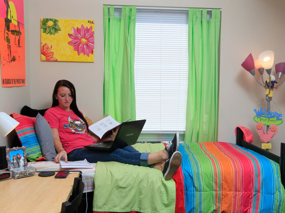 Female student studies on bed in dorm room.