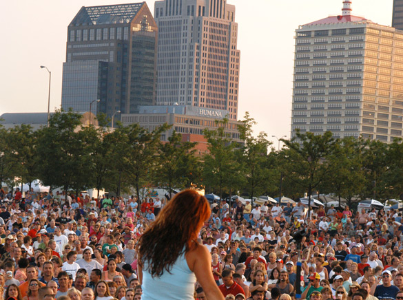 Musician performs for crowd of people at outdoor concert at Louisville Waterfront Park.