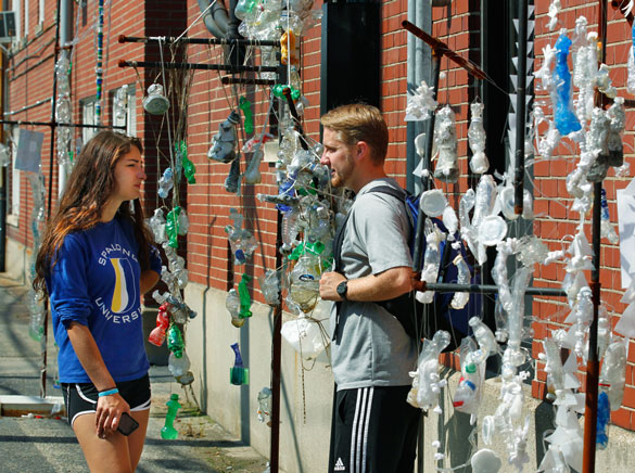 Students outside talking under an art installation of recycled items.