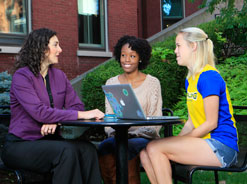 Spalding students and professor sitting outside with laptop