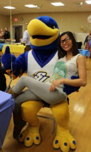 A female student poses for a picture by sitting in the lap of Spalding's large blue and gold eagle mascot