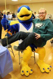 A student poses for a picture by sitting in the lap of Spalding's large blue and gold eagle mascot