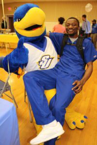 A student poses for a picture by sitting in the lap of Spalding's large blue and gold eagle mascot