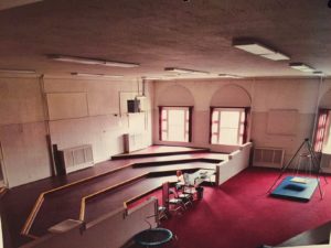 A look at the old College Street Center band room with bright red carpet and wooden risers before it was converted to the Virtual Immersive Playground