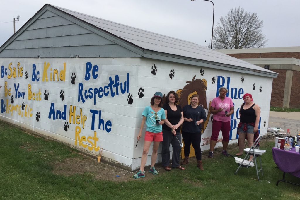Five women stand in front of a building mural at Blue Lick Elementary that they helped paint.