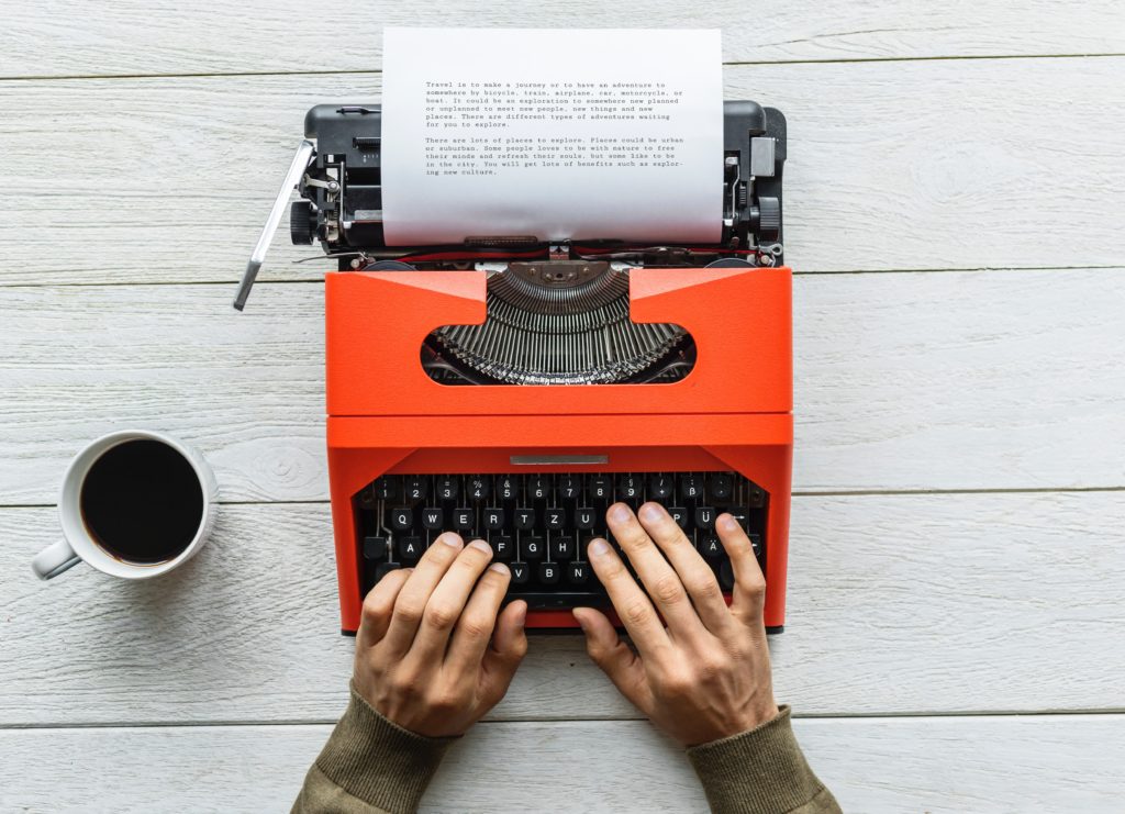 Stock photo of hands typing on orange and black typewriter with cup of coffee next to it