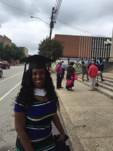 Kendra Unseld, wearing graduation cap, outside in front of library