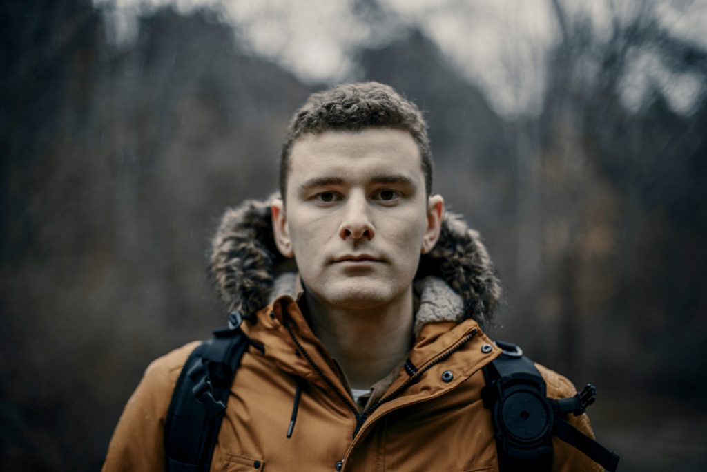 Head shot of Tyler Glass, outdoors, wearing brown hooded jacket