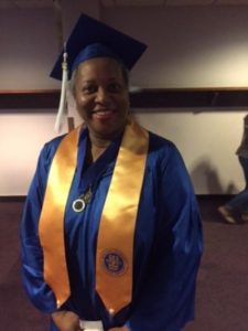 Carla Johnson, smiling, wearing blue cap and gown with gold sash