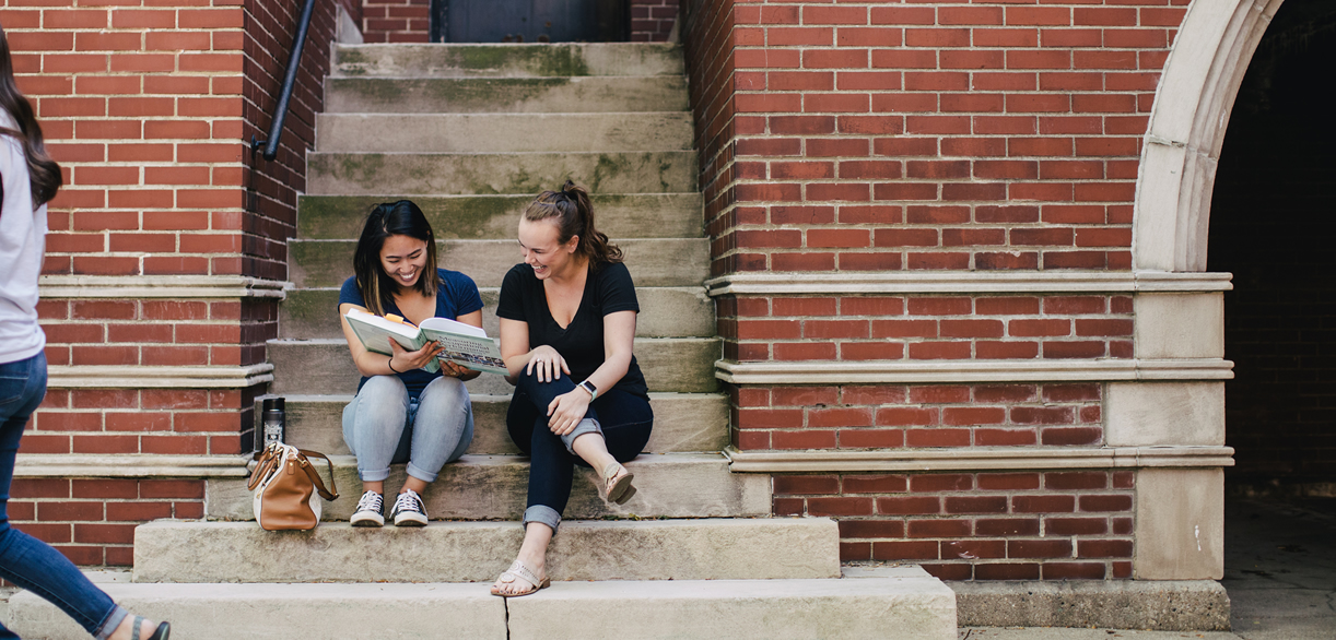 two students sitting on steps read textbook