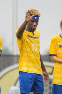 Spalding soccer player Kornell Hilliard, wearing yellow jersey and blue head band, waves during starting lineups