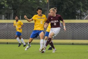 Two opposing soccer players, Spalding's Tenko Kono on the left and a player from Alma on the right, compete to control the ball