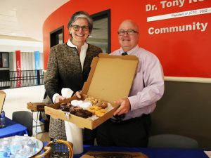 Tori Murden McClure and Ty Handy smile and hold a box of donuts they're distributing to students