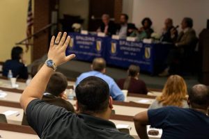 An audience member raises his hand to ask a question to the on-stage panel