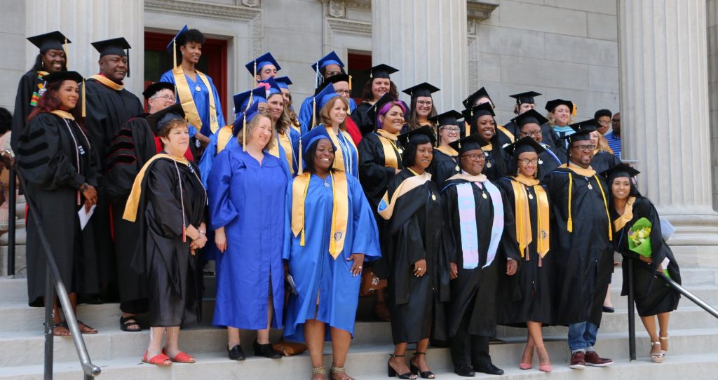 Group of Spalding social work grads and faculty, wearing black and blue graduation regalia, pose outside on building steps