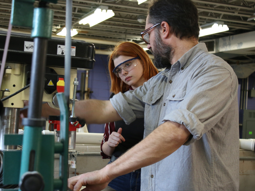 Spalding faculty Shawn Hennessey demonstrates a wood saw cut to student Sarah Thornsberry.