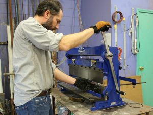 Spalding Professor Shawn Hennessey uses a metal cutter in the Spalding Maker Space