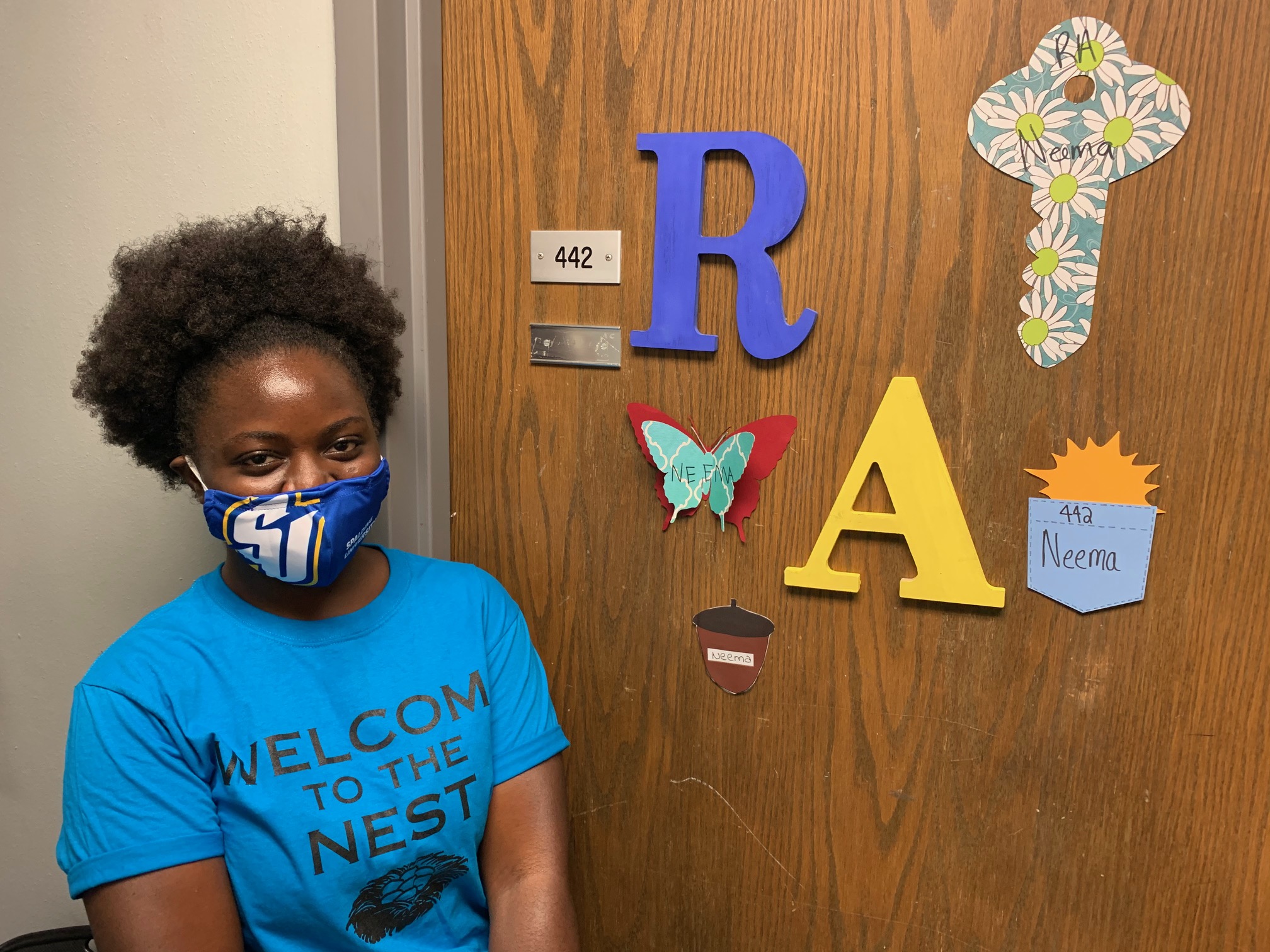Young woman wearing mask in front of her Morrison Hall room