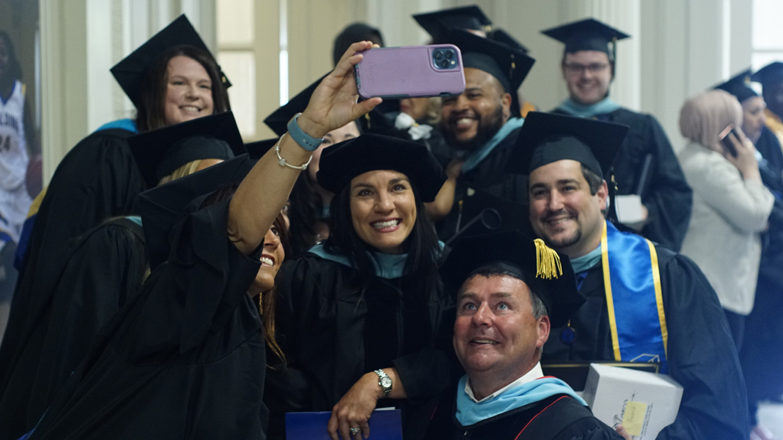 Spalding grads with professor taking selfie in hall before ceremony