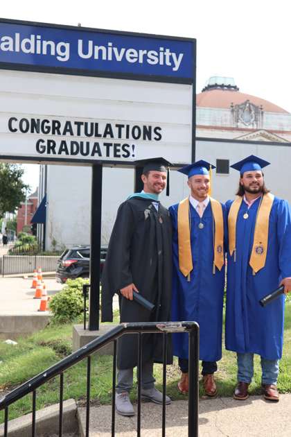 3 Spalding grads with congrats grads sign