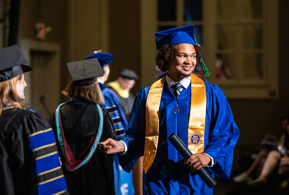 Spalding grad with his degree tube in hand smiling during ceremony