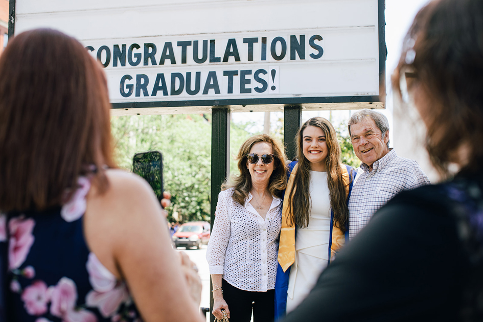 Spalding grad with parents outside in front of congrats grads sign