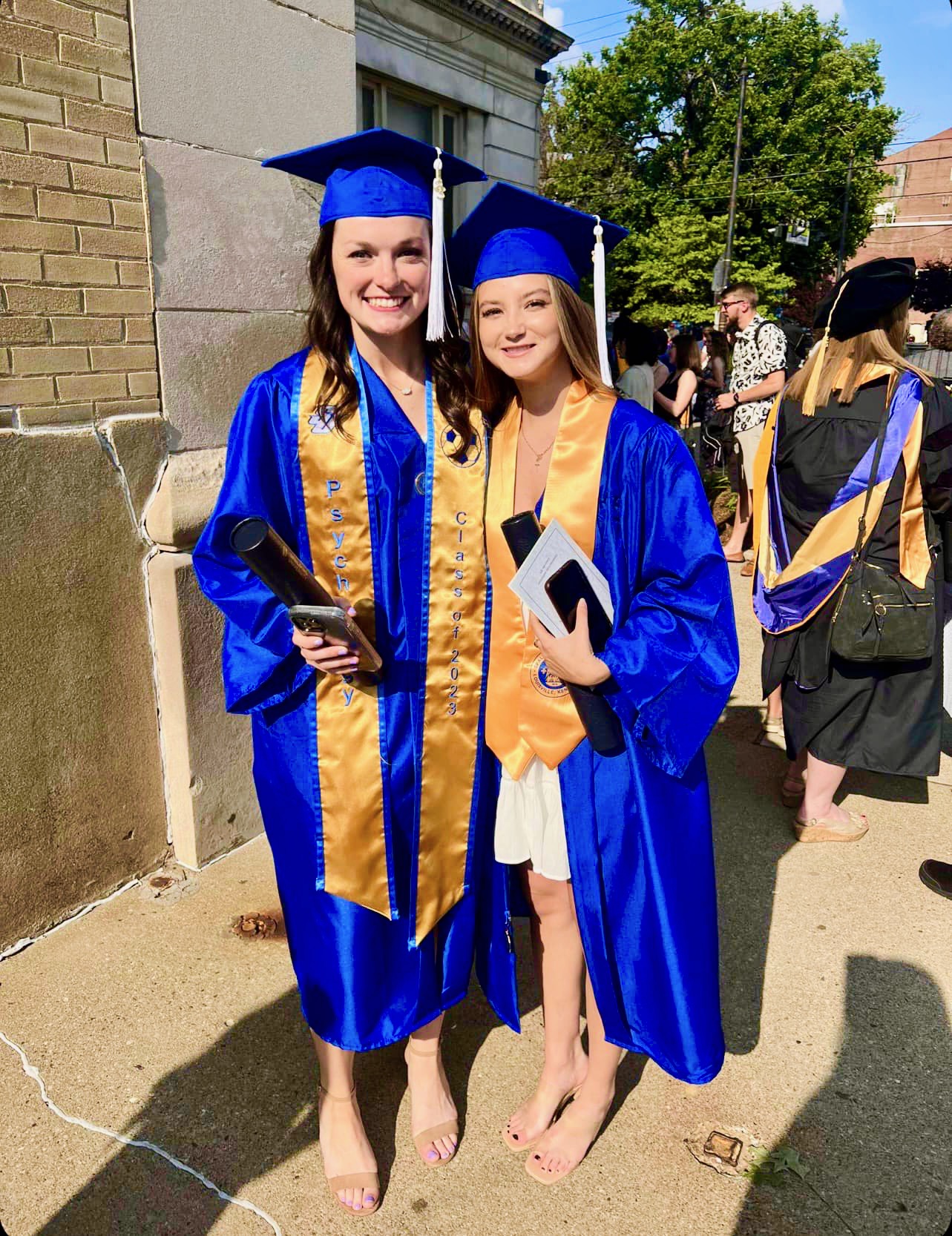 Two Spalding bachelor's graduates in cap and gown posing outside Columbia Gym