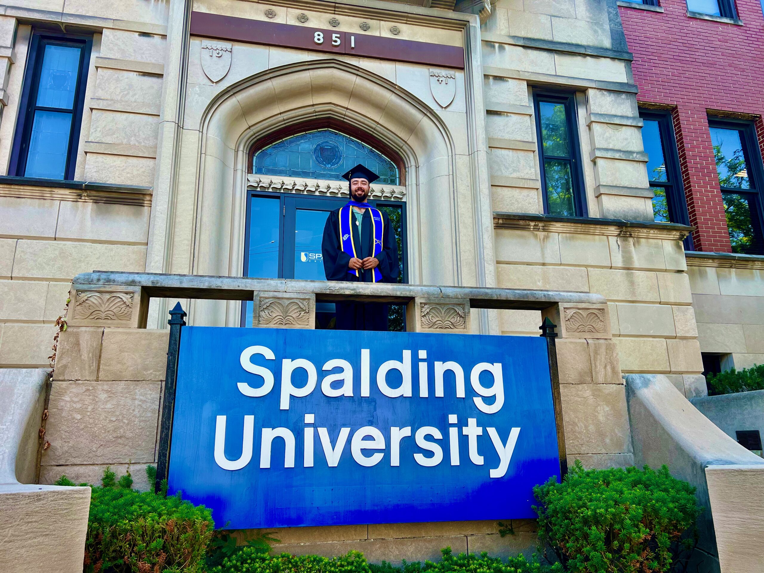 Spalding master's graduate behind Spalding University sign at the mansion's front doors
