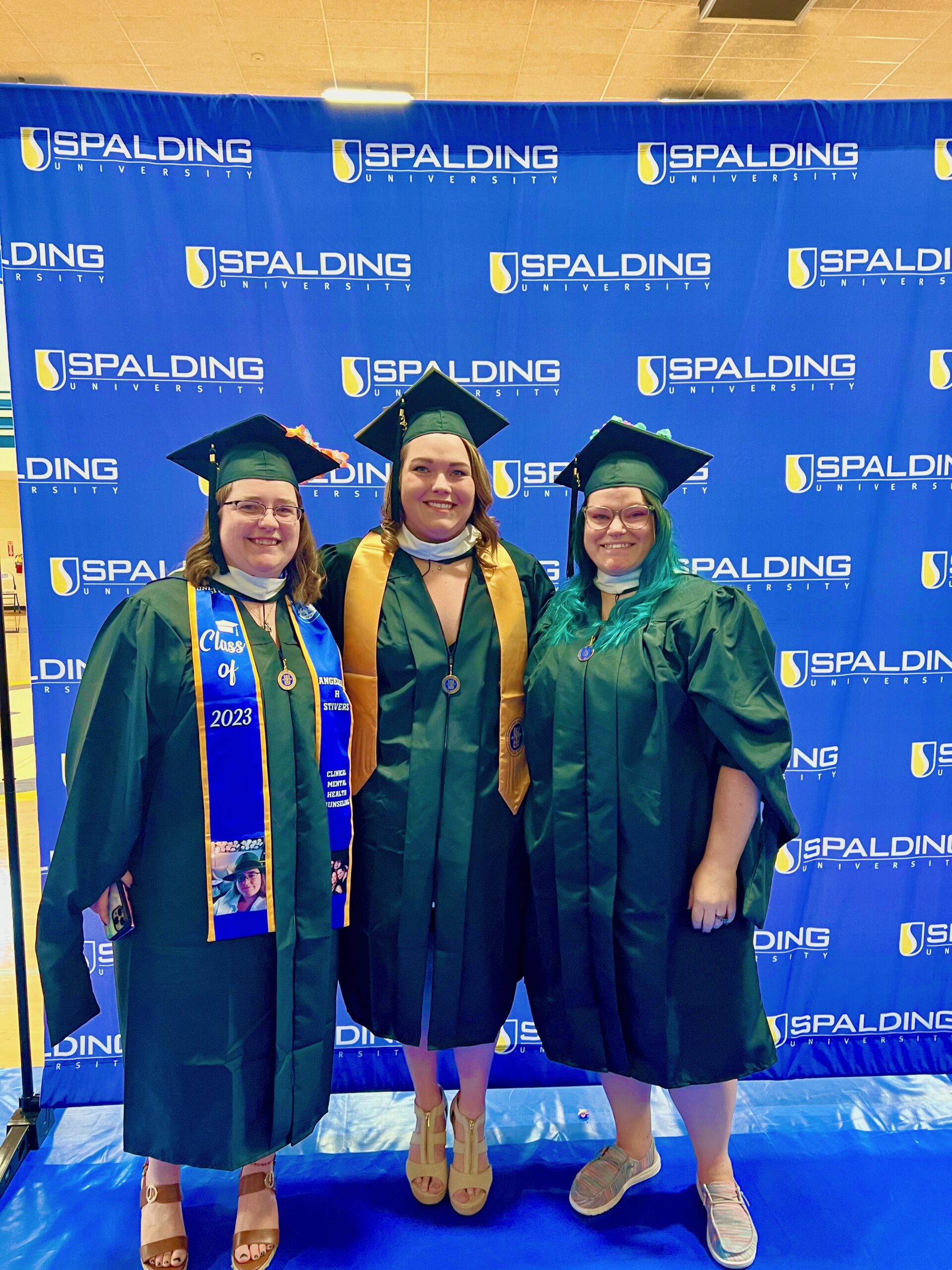 Three Spalding master's graduates posing in front of Spalding backdrop