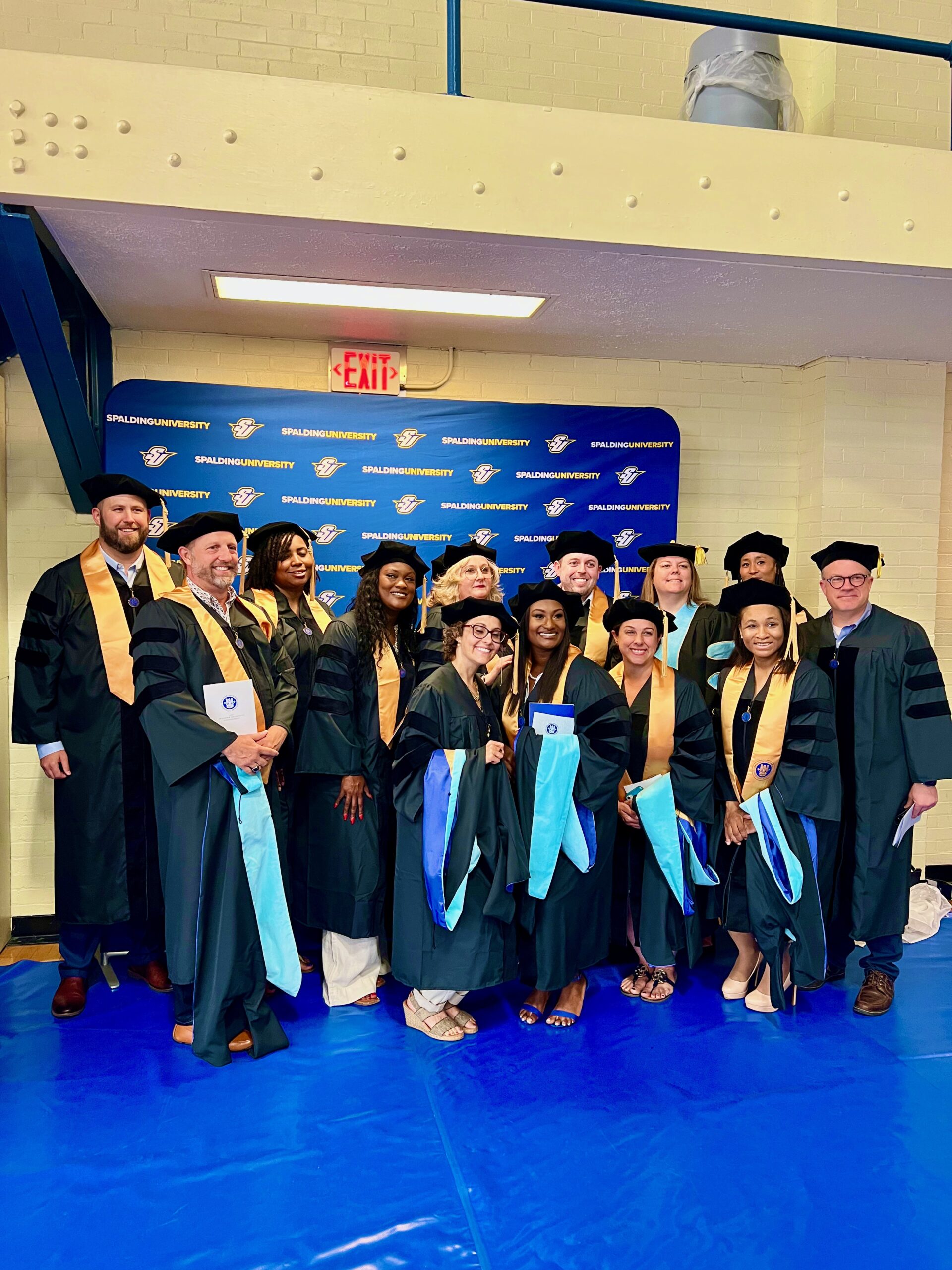 Group of Spalding master's graduates posing for picture in Columbia Gym with Spalding Athletics backdrop