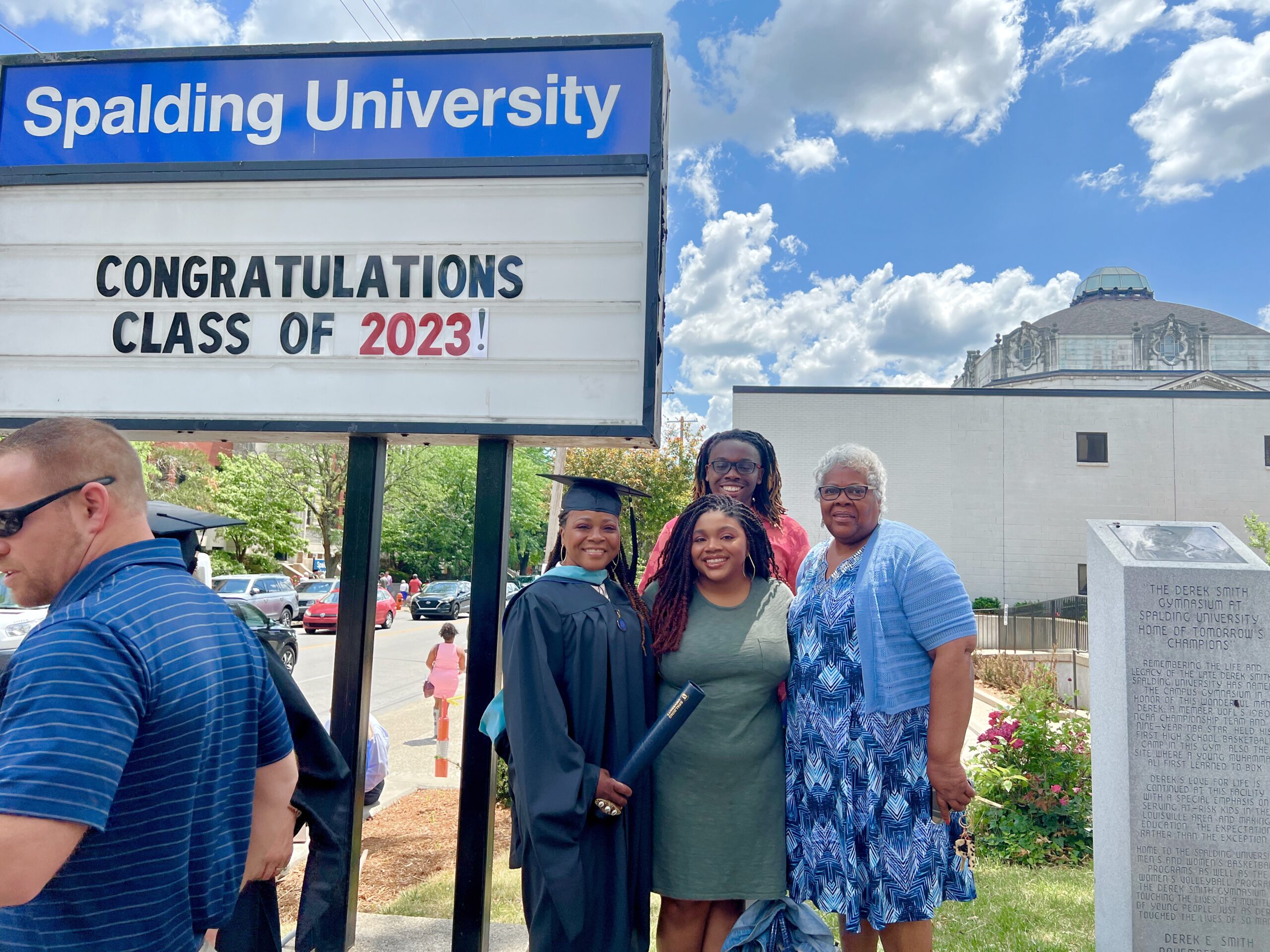 Spalding master's graduate posing with family outside Columbia Gym by sign reading "Congratulations Calss of 2023"