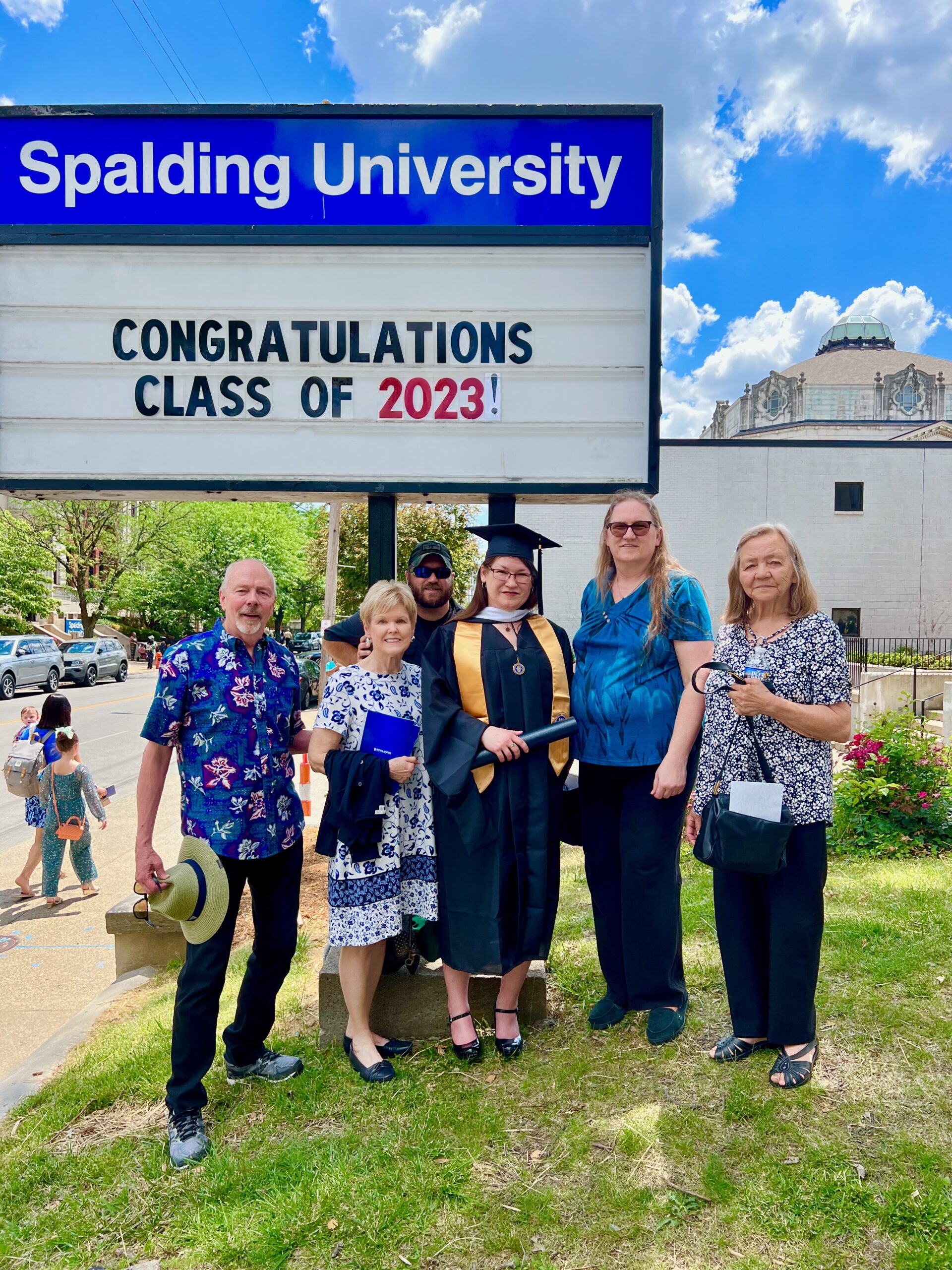 Spalding master's graduate posing with family outside Columbia Gym in front of sign reading "Congratulations Calss of 2023"