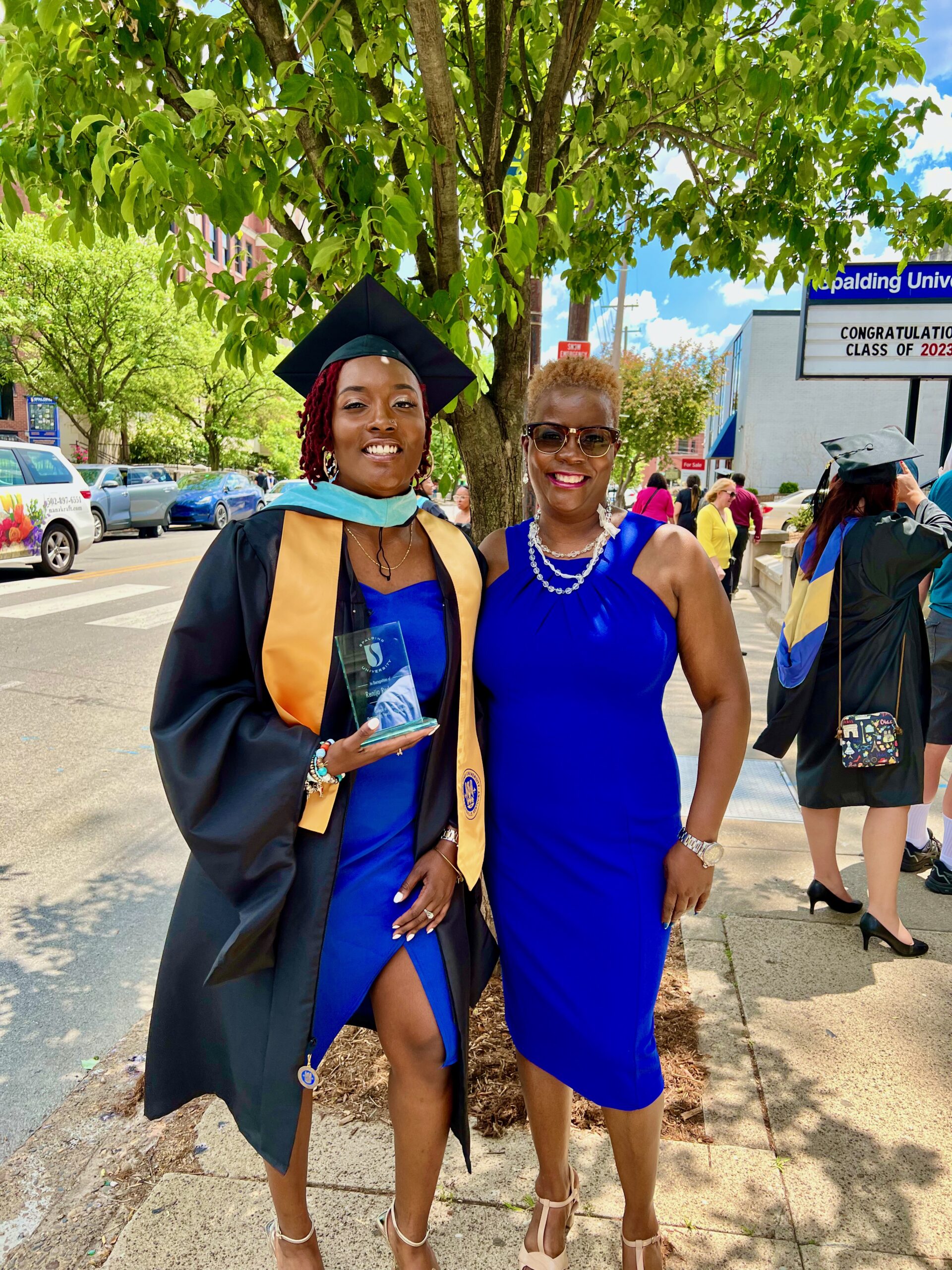Spalding master's graduate posing with mom on sidewalk in front of Columbia Gym
