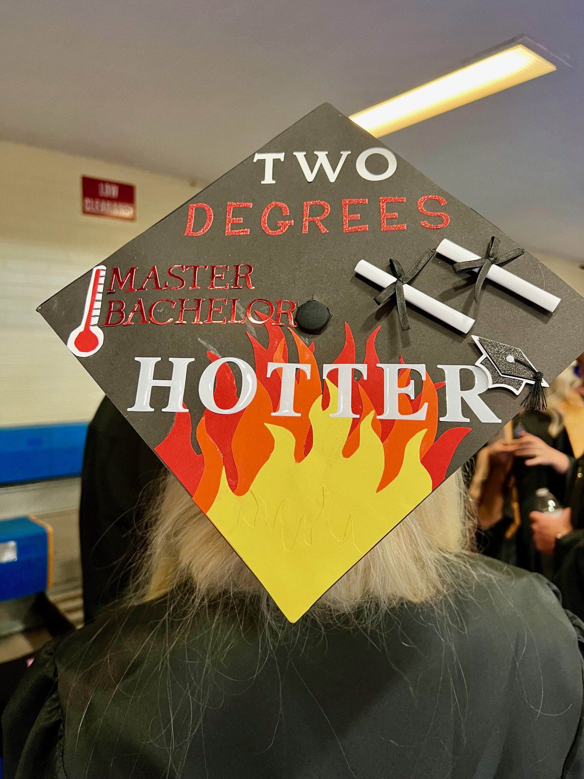 Decorated mortarboard reading "Two degrees hotter, bachelor's masters" with flames at the bottom corner
