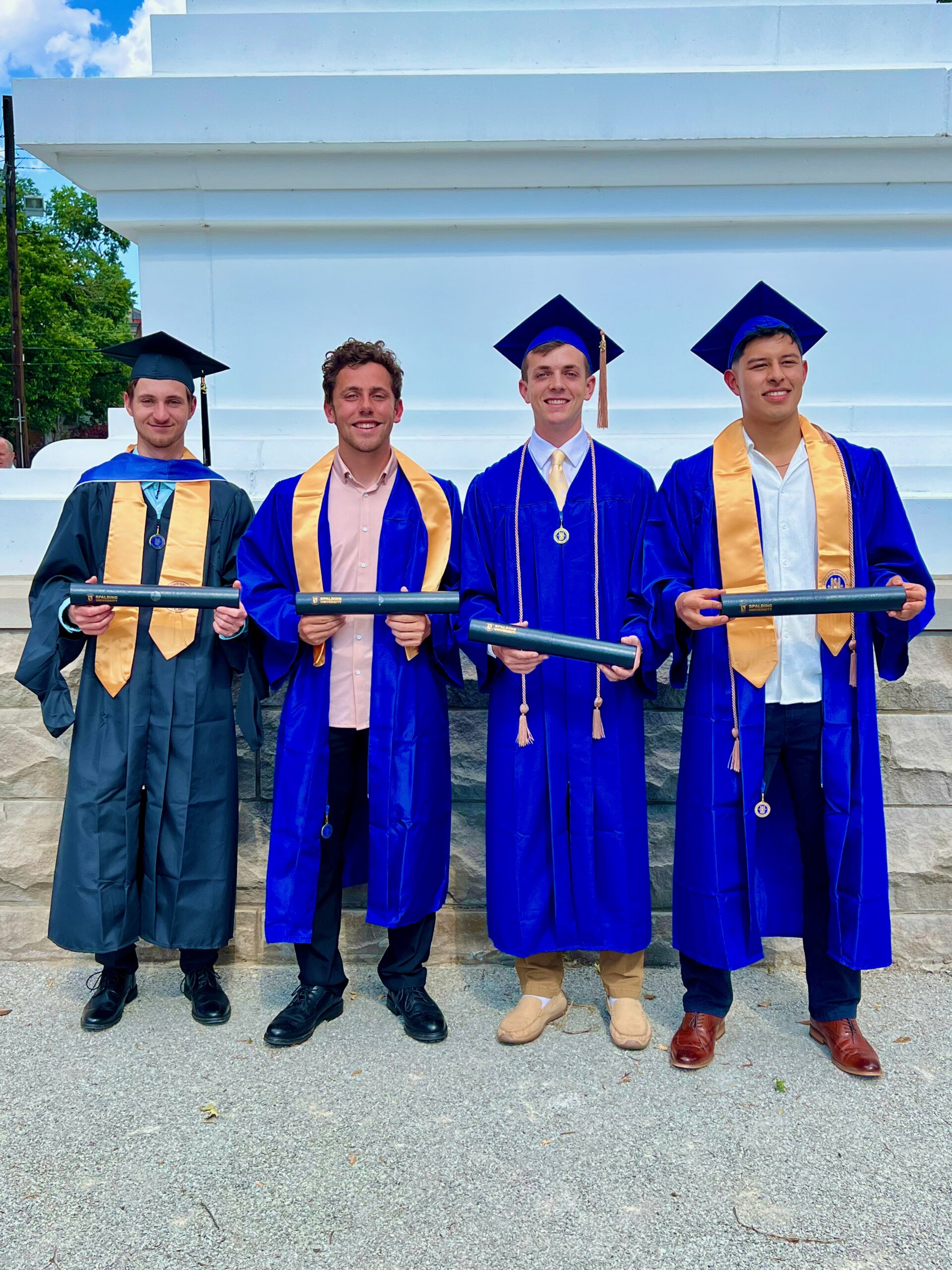 Four Spalding graduates, three bachelor's and one master's, posing with their degree tubes outside