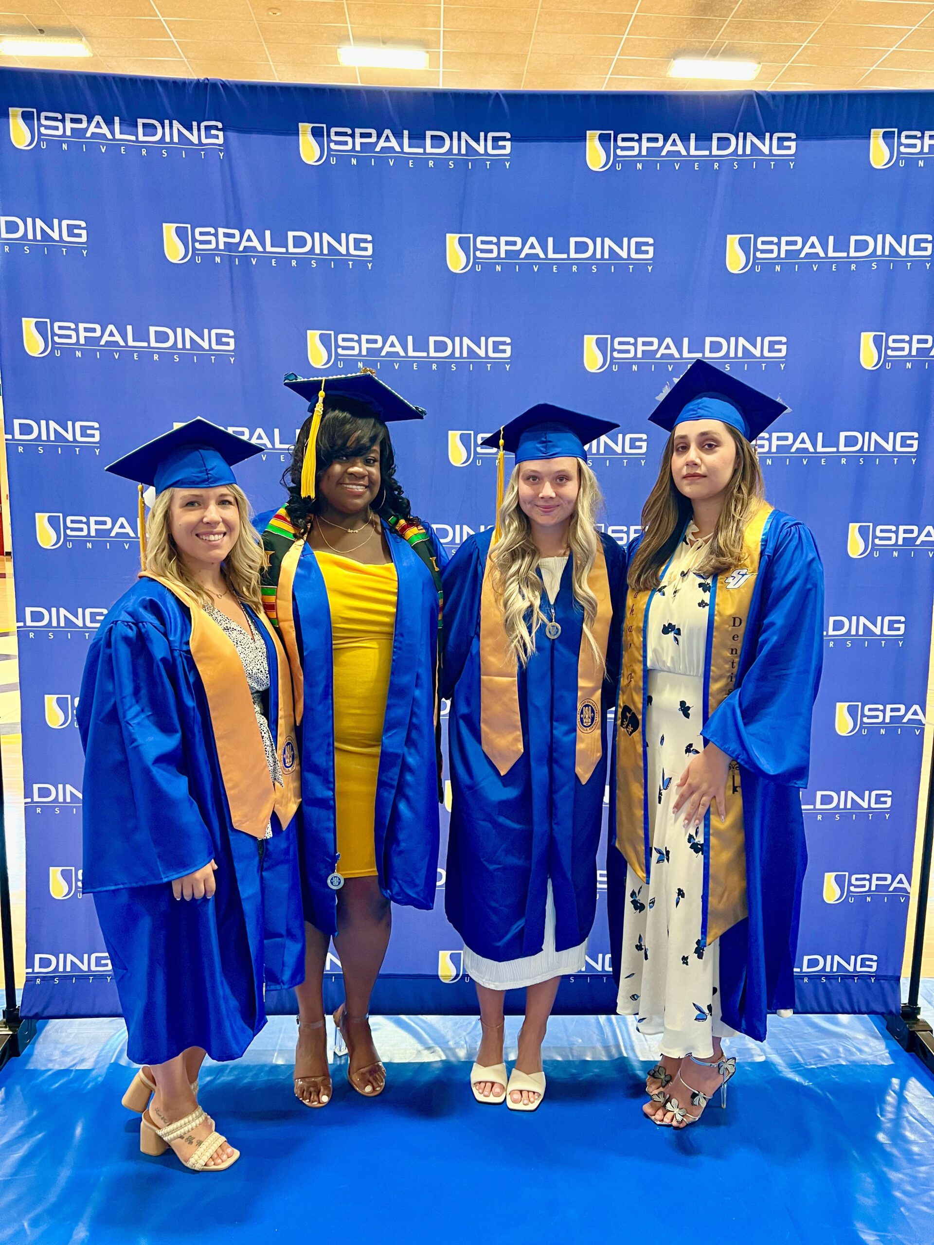 Four Spalding bachelor's graduates posing in front of Spalding backdrop