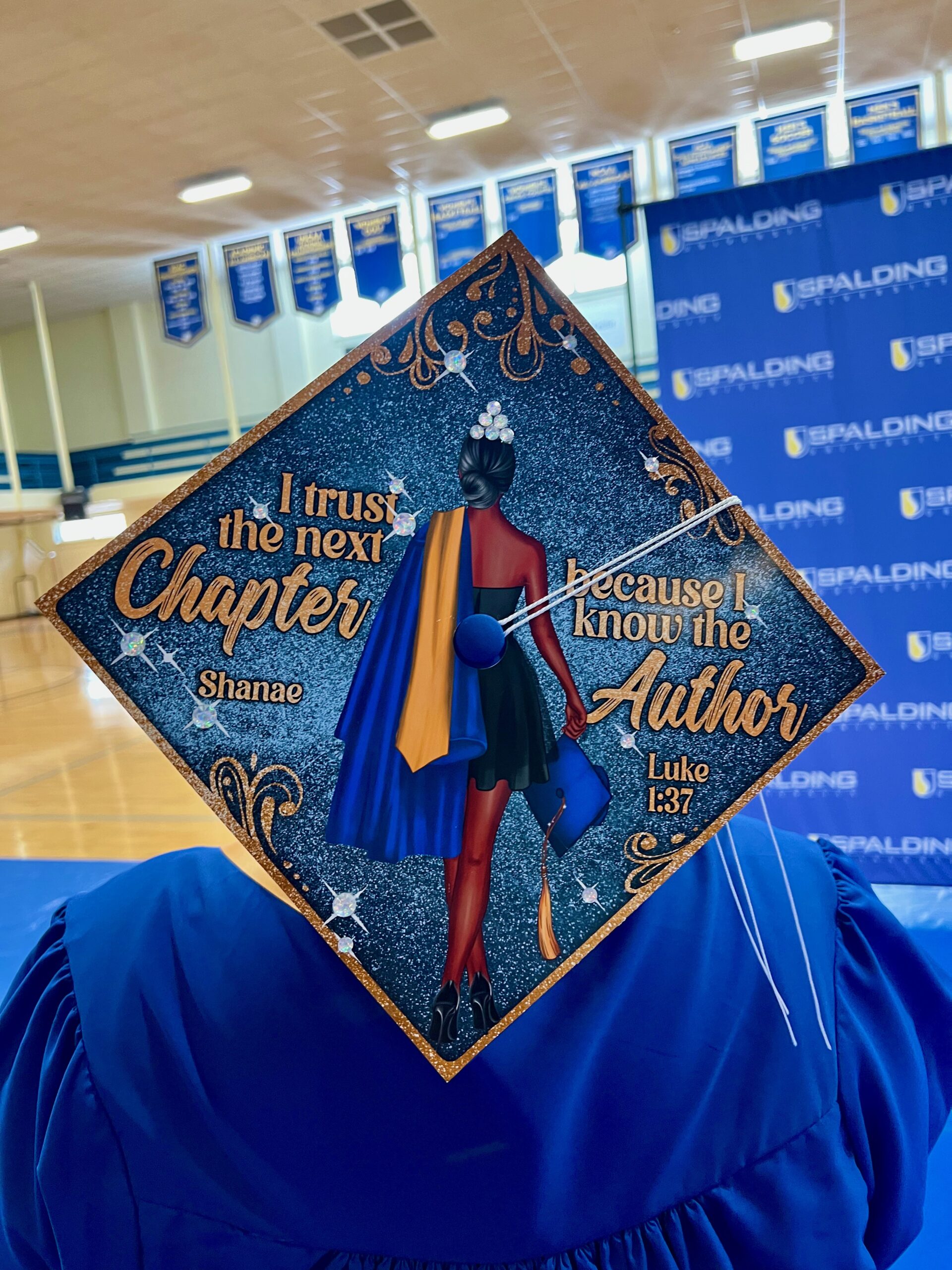 Decorated mortarboard reading "I trust the next chapter because I know the author Like 1:37" with picture of the back of a woman in a black dress hold a cap and gown