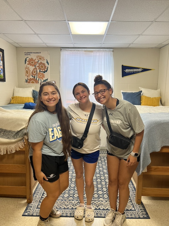 Three female students posing for picture in a dorm room.