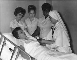 Black and white photo of nursing students with learning from nun working with practice patient