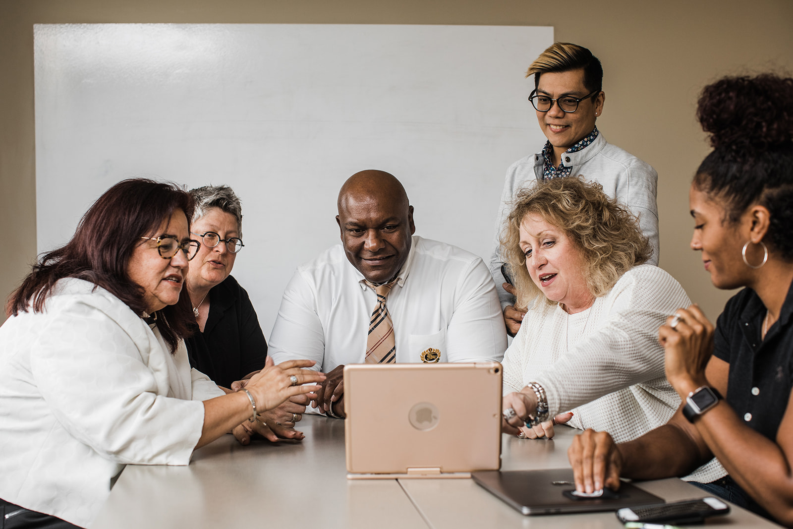 Small group of men and women sit around a table with a laptop in discussion