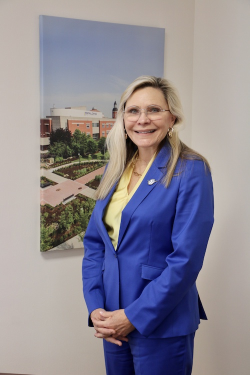 Spalding President Anne Kenworthy in front of photo of aerial view Spalding's campus