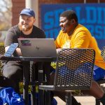 male students sitting at table outside