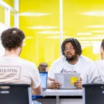 Small group of sudents sits at a table working together in a bright yellow modern room