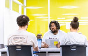 Small group of sudents sits at a table working together in a bright yellow modern room