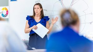 professor in a blue shirt teaching class at whiteboard
