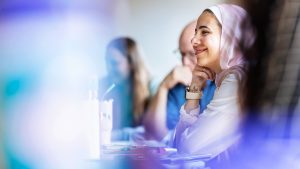 female student in class smiling with hand to chin