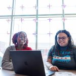 Two black female students visit in front of a laptop computer