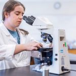 female student in white coat looking at microscope