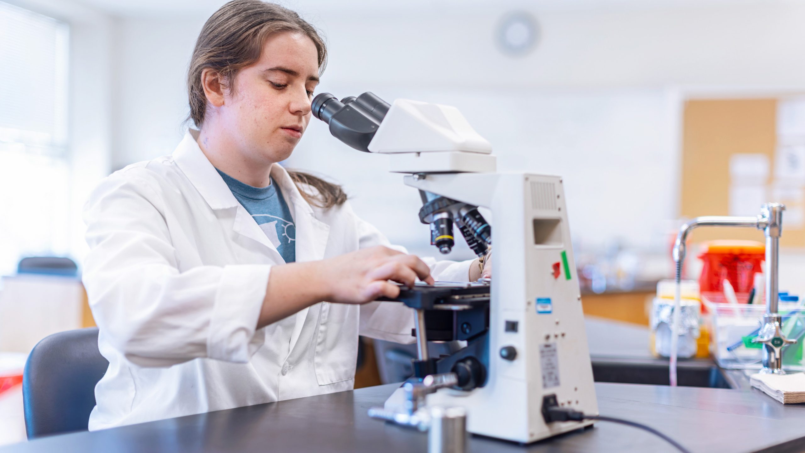 female student in white coat looking at microscope