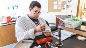 male student in lab coat working in science lab